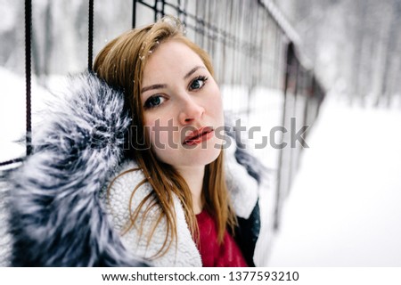 the beautiful girl beside the fence of metal bars amid winter forest