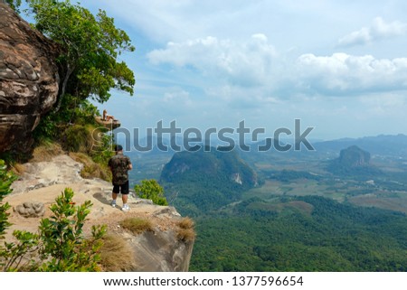 A young photographer takes a picture of a girl from the top of a mountain. Photographs a girl during a risky moment on the edge of a cliff.