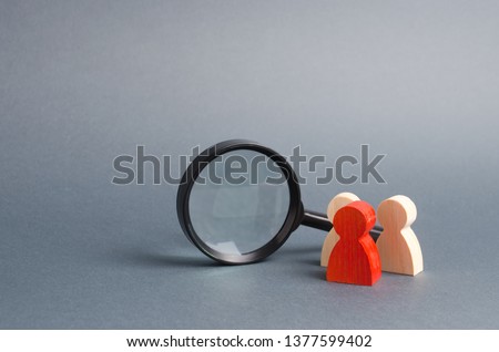 Three wooden human figure stands near a magnifying glass on a gray background. Search for vacancies and work. Human resources, management. The concept of the search for people and workers. Royalty-Free Stock Photo #1377599402