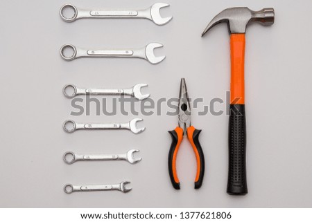 Set of tools contains group of steel silver wrenches, hammer with black and orange handle and pliers over grey background, close-up from above