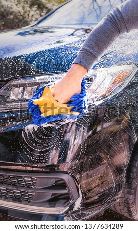 Wash a car on a sunny day. Use a brush and soap to wash a car in the driveway. hand in blurred motion. 