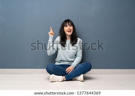 Woman sitting on the floor intending to realizes the solution while lifting a finger up