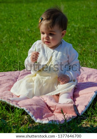 Baby in bright clothes on a pink plaid on green grass in the park. Newborn baby outside on a warm day. Little girl plays on a plaid on a green lawn in spring