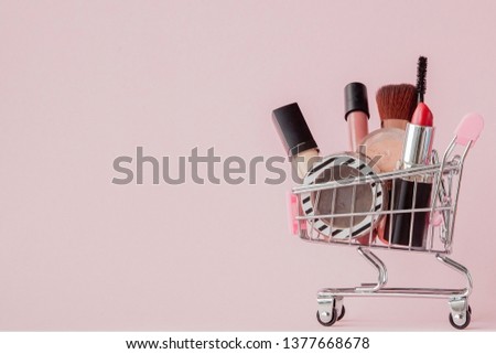 Creative concept with shopping trolley with makeup on a pink background. Perfume, sponge, brush, mascara, pencil, nail file, eye shadow, lip gloss in the basket, copy space. Royalty-Free Stock Photo #1377668678