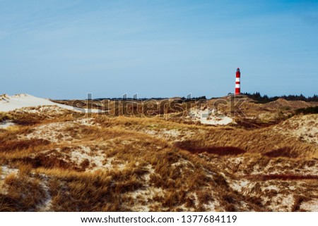 Picturesque landscape with red lighthouse on the hill in distance against cloudy sky and dry grass in foreground. Idyllic view from low angle