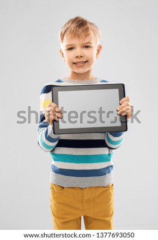 childhood and people concept - smiling little boy in striped pullover showing black screen of tablet pc computer over grey background