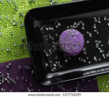 Aerial shot of a purple macaroon on a black plate on a green wooden table
