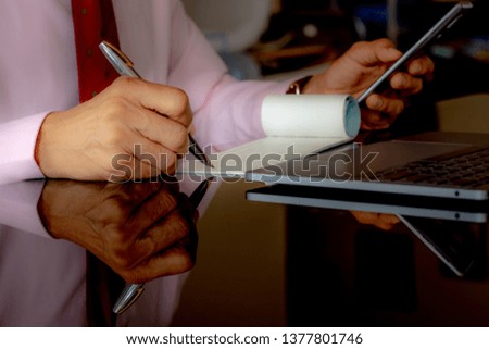 Businessman hand using mobile smartphone , writing and signing  chequebook,work on laptop computer on the desk. Cheque payment concept.