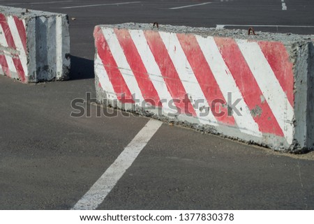 Rows of red and white concrete barriers used in traffic control and safety. Large slab of concrete used as a barrier at a construction site