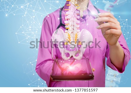 A closeup of physiotherapist with stethoscope pointing at a spine model with pelvis element hanging above a gadget with wireless connections around. The concept of innovative spine diseases treatment.