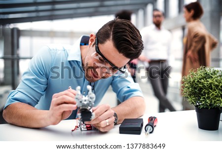 A young businessman or scientist with robotic hand standing in office, working. Royalty-Free Stock Photo #1377883649