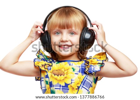 Beautiful little girl listening to music through large stereo headphones. The concept of musical education, advertising of musical goods, CDs of various performers. Isolated on white background.