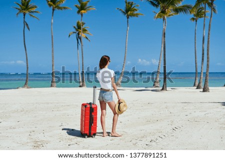 Rear view woman with a suitcase on an island with palm trees tropics sand sea                              
