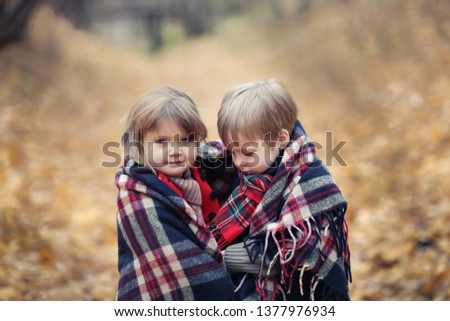 Frozen children in the autumn forest bask under a warm blanket, a boy and a girl warm themselves with tea in the park, cozy pictures for postcards