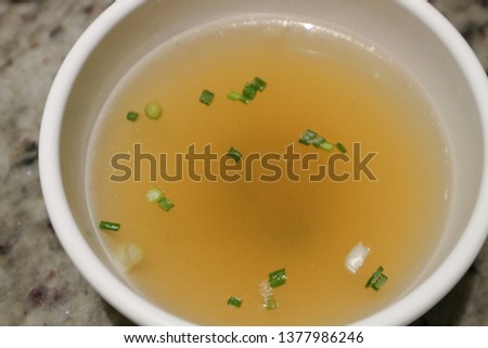 Top view of tasty meat broth soup with herbs in a white bowl