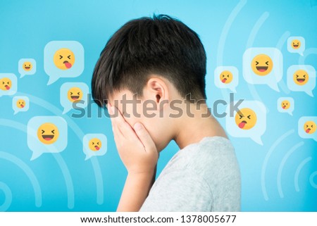 Cyberbullying CONCEPT - A preteen / teen asian boy hands cover his face feeling hurts and stressed from ONLINE 'SOCIAL MEDIA' bullying. Blue background with graphic. Royalty-Free Stock Photo #1378005677