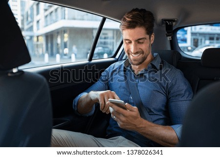Happy smiling business man typing message on phone while sitting in a taxi. Young businessman in formal clothing using smartphone while sitting on back seat in car. Cheerful guy messaging with cell. Royalty-Free Stock Photo #1378026341