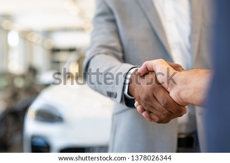 Closeup of a salesman shaking hands with his client after selling him a car at the dealership. Handshake between customer and african car dealer at automobile showroom. Royalty-Free Stock Photo #1378026344