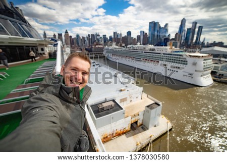 Young man makes selfie with huge cruise ship and New York city on background. Concept of happy vacation and travelling