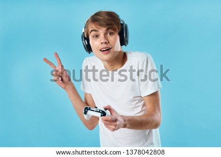Teenager in the headphones shows two fingers and holds the joystick in his hand                              
