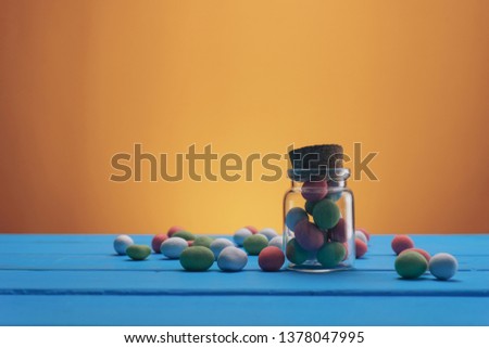 Small bottle of multicolored peanuts in chocolate and icing. Blue wooden table and yellow background. Macro view.