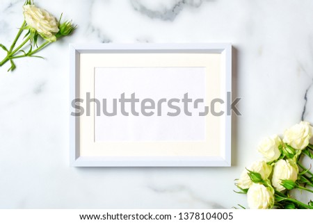 Anniversary congratulation flower background. White rose and frame with blank paper card on marble background, flat lay composition, top view, overhead.