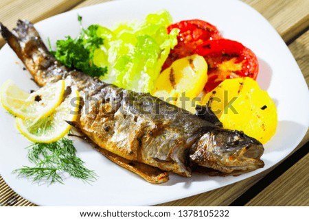 Picture of  tasty baked whole  trout  with potatoes, greens and tomatoes on white plate