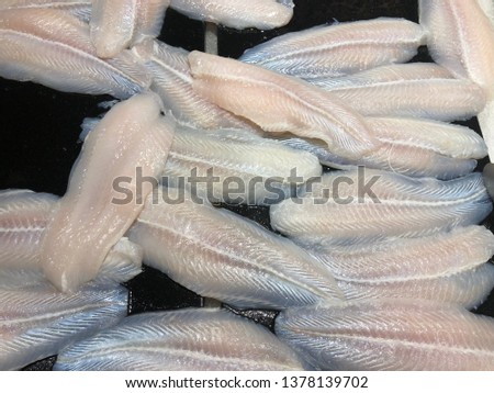 Sliced Dory Fish for sell in market Frozen Dory Fish Fillets Sliced raw Saba fish with metallic grip on black rocky tray in a local rural hypermarket Frozen Dory Fish Fillets (Pangasius)