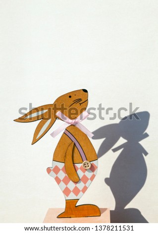 Figure from wood. Silhouette of a dressed bunny and his shadow on a white backdrop