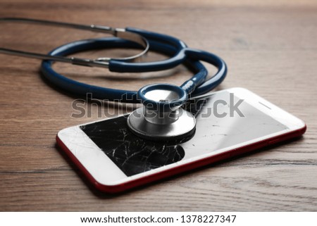 Modern smartphone with broken display and stethoscope on wooden table, closeup. Device repair service