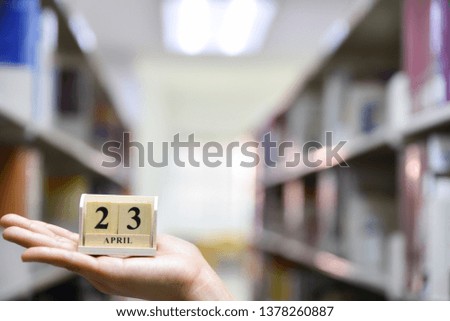 Woman hand holding April 23 text wooden block calendar on bookshelf background. World Book and Copyright Day concept.