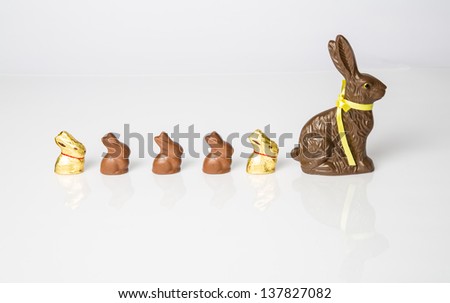 Large Chocolate Easter bunny with smaller chocolate bunnies lined up in a row. Studio Isolated on white with reflection. Part of a Series.