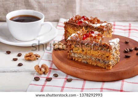 a piece of cake with caramel cream and poppy seeds on a wooden kitchen board and a cup of coffee, close up, white background.