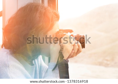 Young girl taking photo of amazing landscape sunset with DSLR camera behind the train window