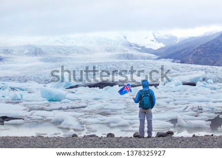 travel to Iceland, tourist in Jokulsarlon glacier lagoon holding icelandic flag, backpacker trip