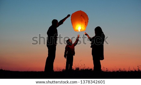 Parents, child and baby silhouette rising lightning sky lantern, release hope