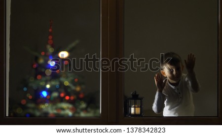 Funny child look careful on window in the night for Santa Claus, Christmas tree