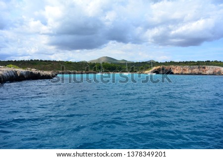 The view from the tourist boat on the rocky shore and the blue clear water of the Mediterranean Sea and three yachts standing in a row in the bay. East coast of the Spanish island of Mallorca