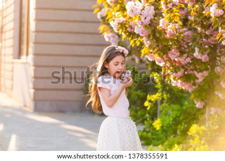 Spring portrait, adorable little girl in hat walk in blossom tree garden on sunset