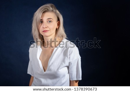 Portrait of young beautiful blonde attractive emotional woman is wearing in white, ironic expression. Isolated on dark background. Photo with copy space