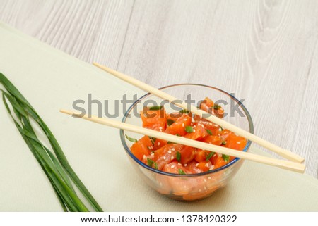 Hawaiian salmon poke with green onions and sesame seeds in glass bowl with chopsticks. Top view. Organic seafood.