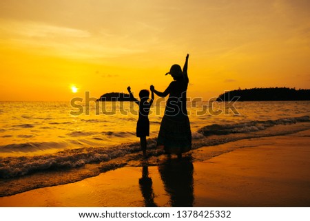 A mother and son playing on the beach and sea outdoors at sunset in happy holiday vacation time with copy space