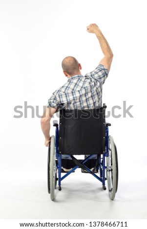 Portrait of caucasian man sitting in a wheelchair, posing with arm raised as a sign of victory. Seen from behind.