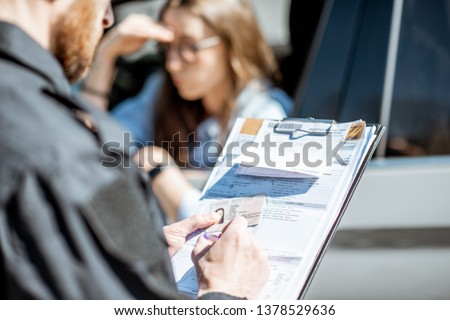 Policeman issuing a fine for violating the traffic rules to a young woman driver, close-up view focused on the folder Royalty-Free Stock Photo #1378529636