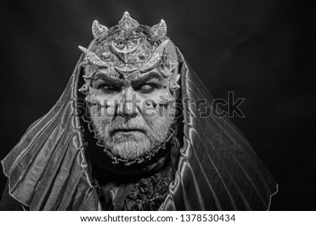 Man with thorns or warts, face covered with glitters. Demon with golden hood on black background. Senior man with white beard dressed like monster. Fantasy concept. Alien, demon, sorcerer makeup.
