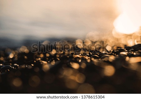 Small stones by the sea with bokeh effect. Blurred decorative vacation and holiday background, place for text. Summer wallpaper, sunny sunset light.