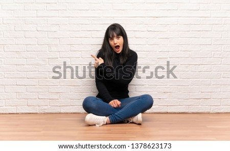 Woman sitting on the floor surprised and pointing side