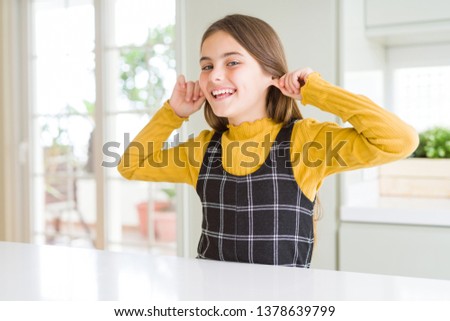 Young beautiful blonde kid girl wearing casual yellow sweater at home Smiling pulling ears with fingers, funny gesture. Audition problem