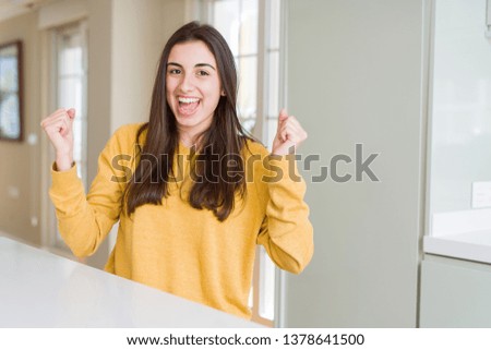 Beautiful young woman wearing yellow sweater celebrating surprised and amazed for success with arms raised and open eyes. Winner concept.