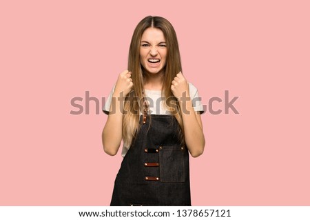 Young woman with apron frustrated by a bad situation on isolated pink background